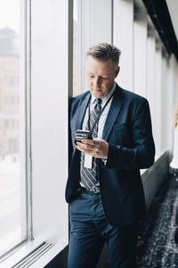 Entrepreneur using phone while standing by window in office