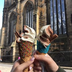 Cropped hands of friends holding ice cream cone against historic building