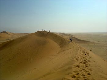 People walking on sand dune in desert against sky