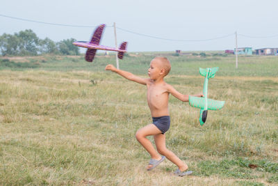 Cute little boy in shorts runs across the field and launches a toy airplane.