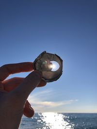 Hand holding sea against clear sky