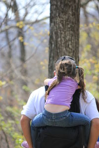 Rear view of man piggybacking daughter in forest