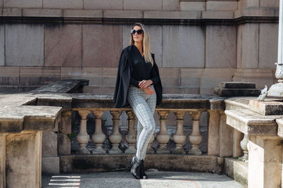 Woman wearing sunglasses looking away while standing against building