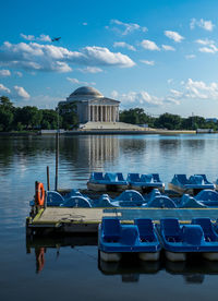 Blue boats in lake by building against cloudy sky