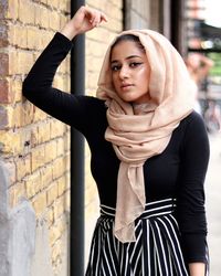 Portrait of young woman standing against brick wall