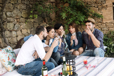 Happy friends drinking wine at party against stone wall