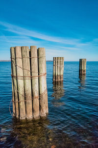 Wooden posts in sea against sky