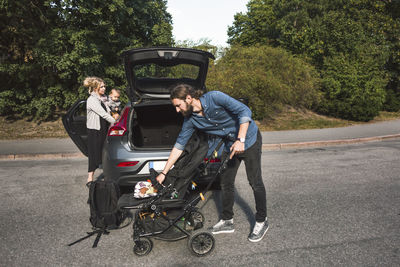 Mid adult parents with baby boy and stroller near car on street