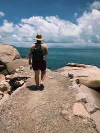 Rear view of man walking on sea shore against sky