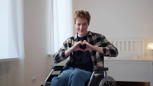 Portrait of smiling man sitting on wheelchair while making heart shape