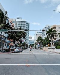 City street by palm trees and buildings against sky