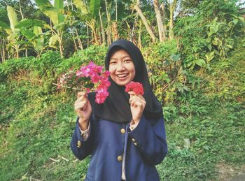 Portrait of happy woman holding flowers against trees