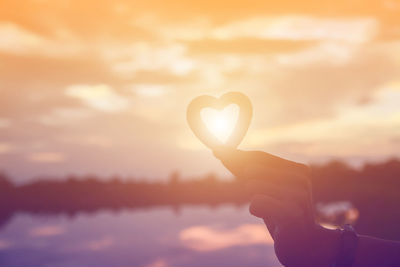 Silhouette hand holding heart shape against sky during sunset