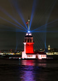 Lighthouse by sea against sky at night