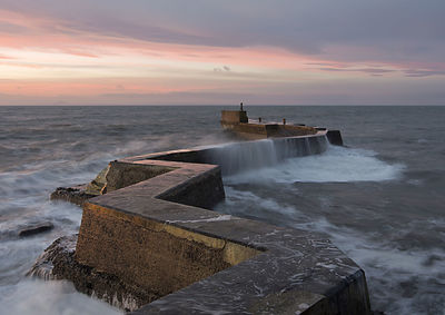 Groyne on sea against sky during sunset