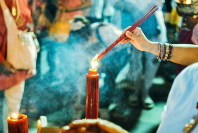 Low angle view of hand holding lit candles in temple