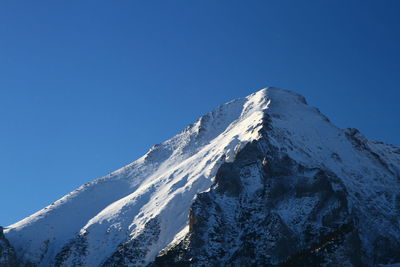 Low angle view of snowcapped mountains against clear blue sky