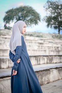 Young woman standing with arms outstretched against built structure