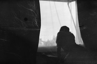 Rear view of silhouette woman standing against window