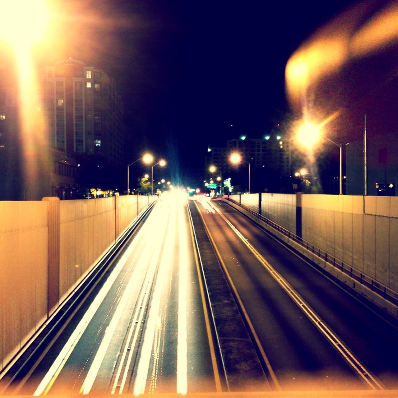 illuminated, night, transportation, long exposure, street light, light trail, the way forward, motion, speed, lighting equipment, diminishing perspective, city, blurred motion, vanishing point, built structure, architecture, building exterior, light - natural phenomenon, railroad track, road