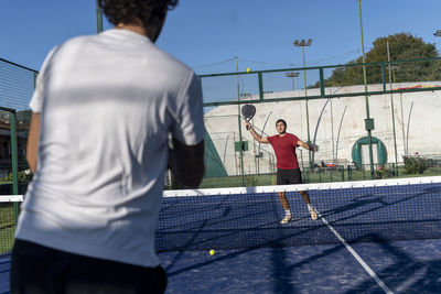 Young man with friend playing paddle tennis at sports court on sunny day