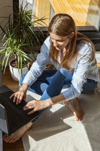 A young girl sits at home by the window at a laptop and types, writes. online communication.