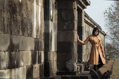 Muslim tourist woman wearing hijab / headscarf and brown coat at ratu boko temple, yogyakarta