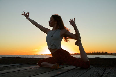 Low angle view of woman with arms raised against sky during sunset