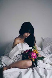 Naked woman with bouquet relaxing on bed at home