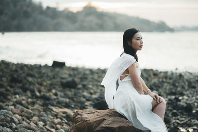 Side view of young woman sitting on rock at beach