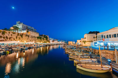 Boats moored in canal by buildings against clear blue sky