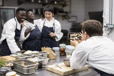Chef photographing cheerful colleagues at restaurant kitchen