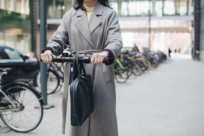 Midsection of businesswoman riding electric push scooter on footpath in city