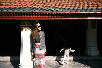 Portrait of young woman standing against building