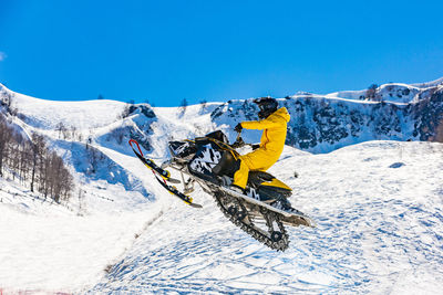 Person riding motor vehicle on snowcapped mountain against clear blue sky