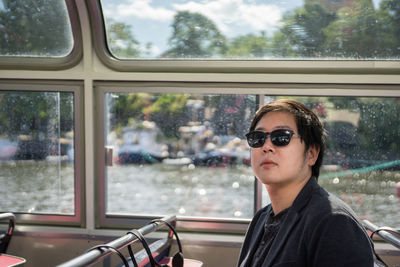 Young man wearing sunglasses sitting by window in bus