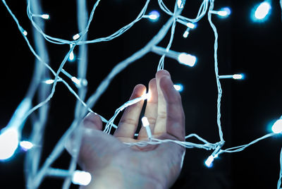 Close-up of hand holding by illuminated string lights against black background