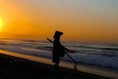 Silhouette person on beach against sky during sunset