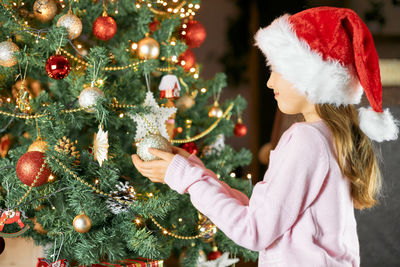 Waiting for the new year and christmas. adorable child decorates a christmas tree in a santa hat.