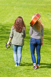 Rear view full length of woman with friend walking on grassy field