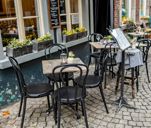 Empty chairs and tables at sidewalk cafe against buildings
