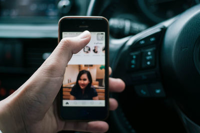 Cropped image of hand holding mobile phone in car