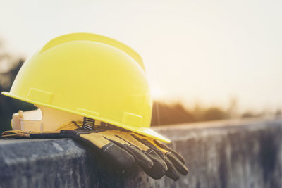 Close-up of protective glove with hardhat on retaining wall against sky during sunset