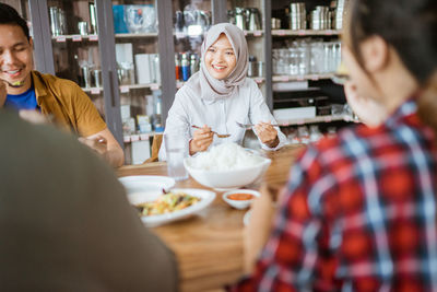 Smiling friend eating food in cafe