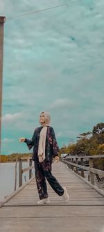 Woman standing on railing against sky
