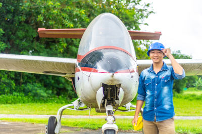 Portrait of engineer standing by airplane against trees