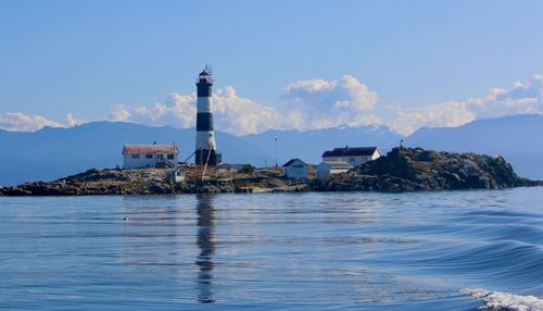 Lighthouse by sea and buildings against sky