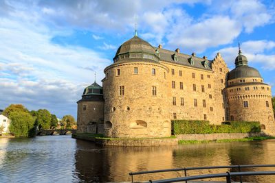  the castle by river against cloudy sky