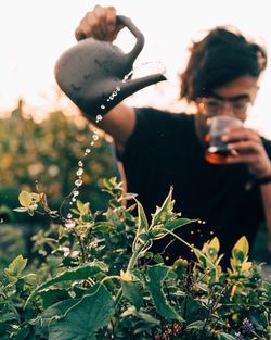 Man pouring water on plant while drinking coffee