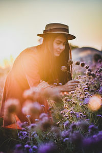 Woman wearing hat touching flower against sky